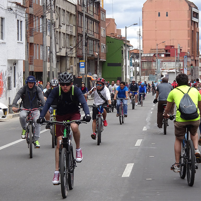 dozens of people ride bicycles down an urban street, several bicycles wide and in both directions